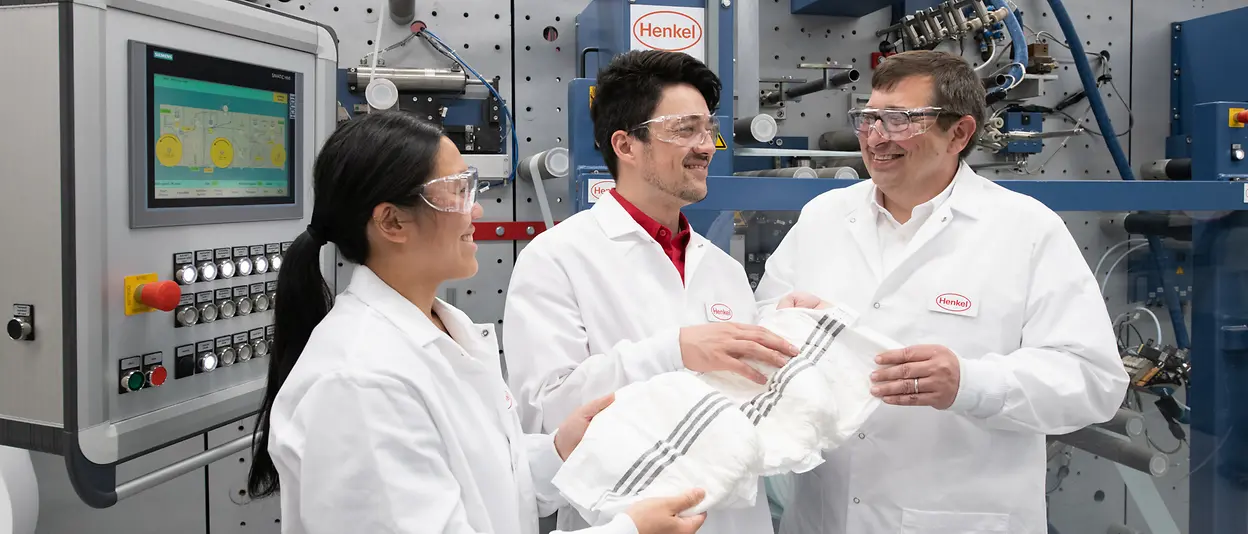 Three R&D experts standing in front of equipment and holding a smart adult care diaper.