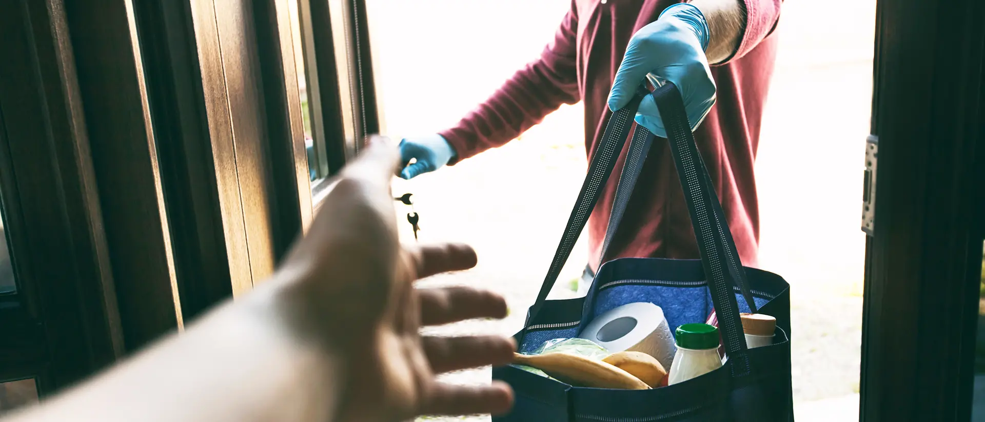 hands reaching over for an offered shopping bag full of groceries