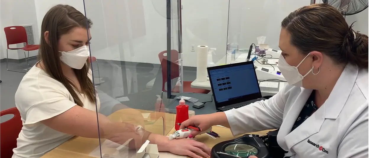 A scientist is applying a clinical test to the skin of a female research candidate.