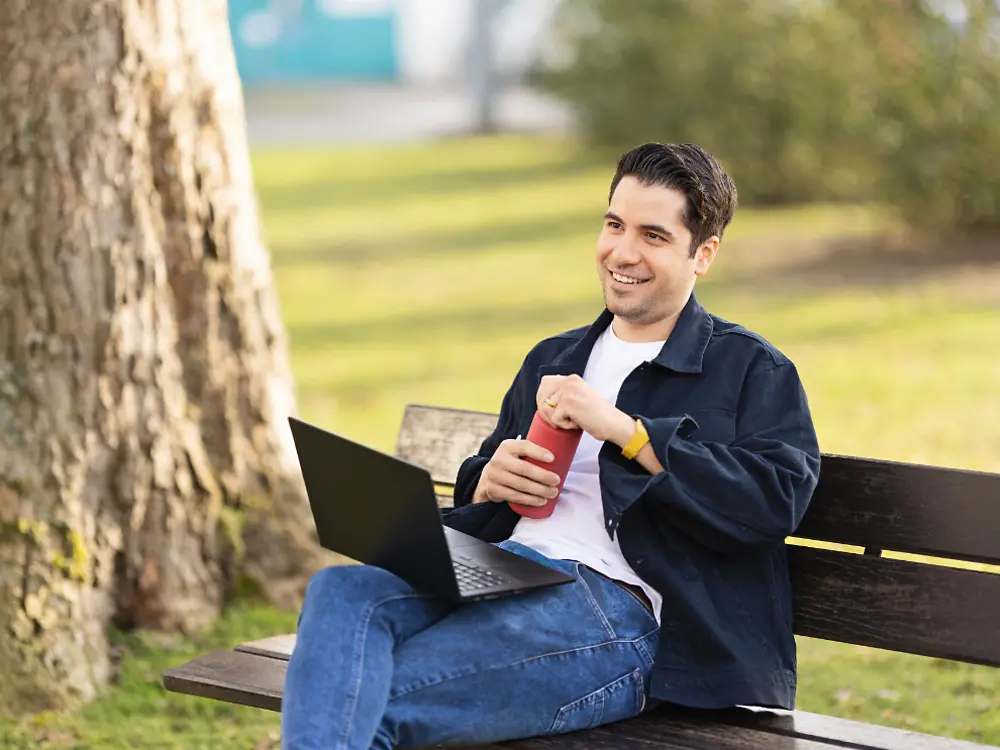 Un employé de Henkel est assis sur un banc dans un parc et travaille sur son ordinateur portable. 