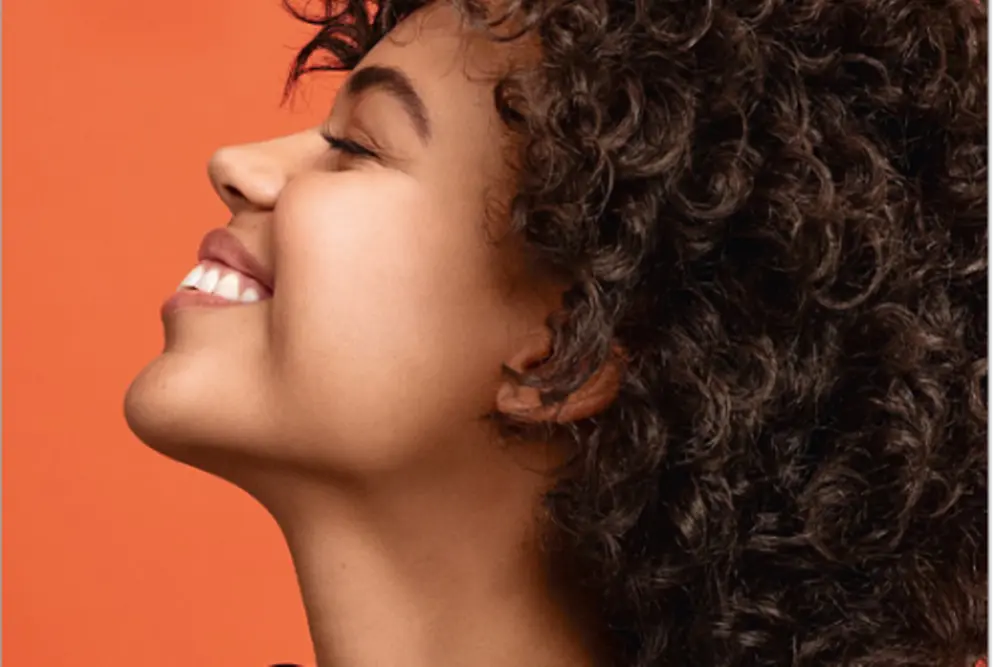 A woman smiling confidently with eyes closed.