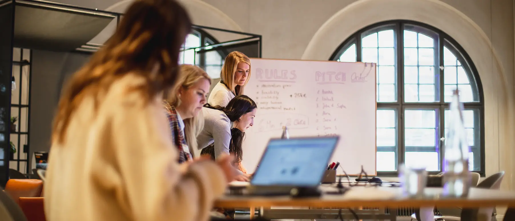 Women work on laptops in front of a flipchart.