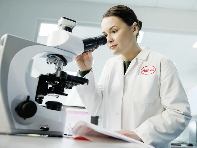 woman in Henkel lab coat looking into a microscope