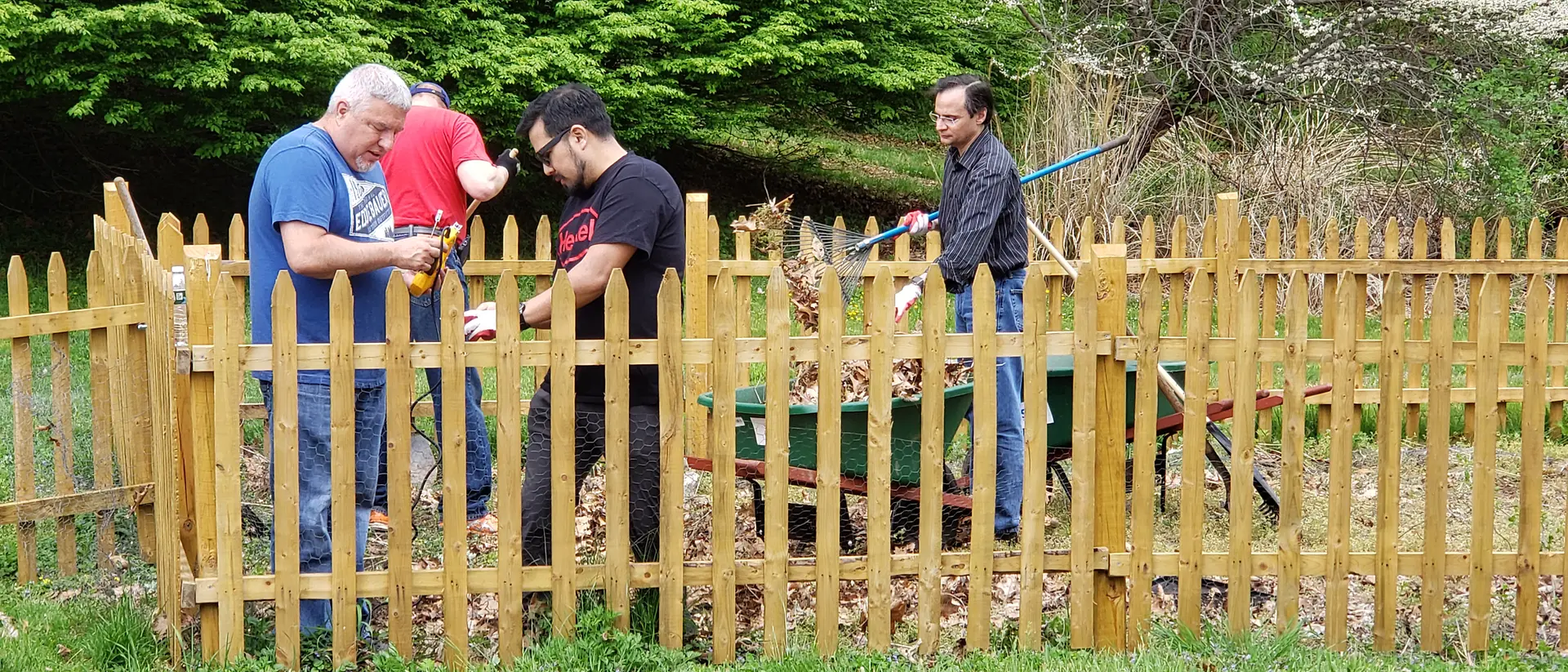 Henkel employees work on cleaning up a yard, with rakes and a wheelbarrow.