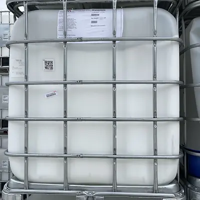 Large white plastic drum in metal caging, stacked among others in a manufacturing facility.
