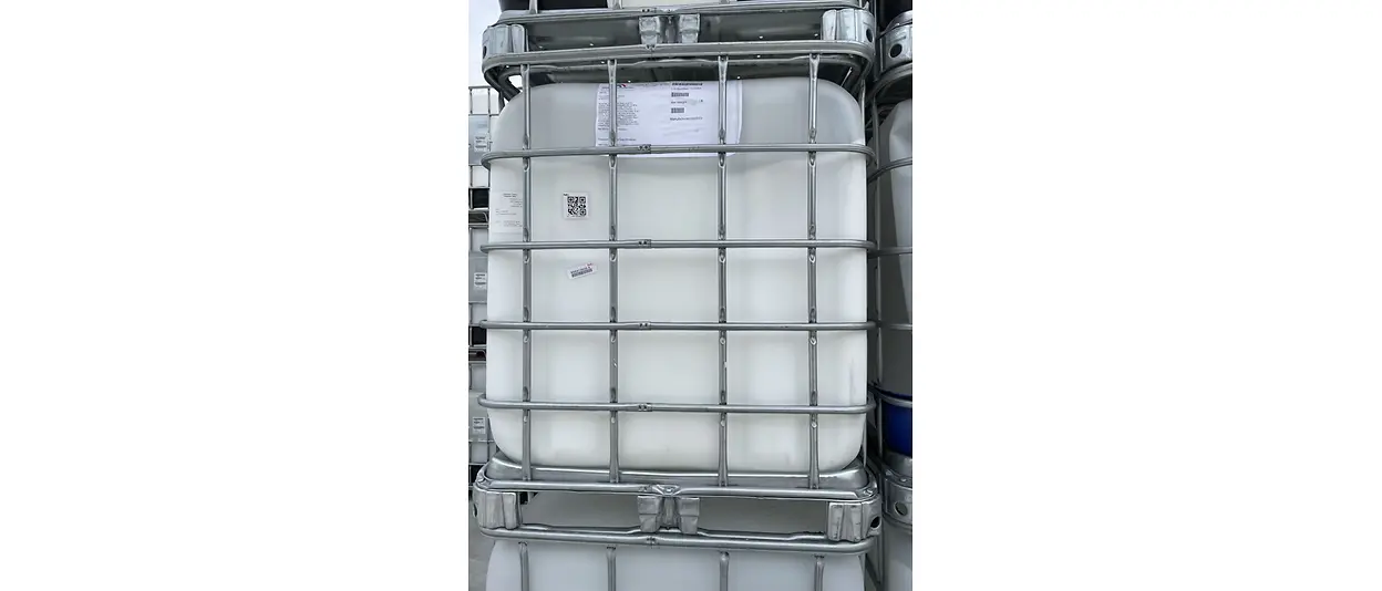 Large white plastic drum in metal caging, stacked among others in a manufacturing facility.
