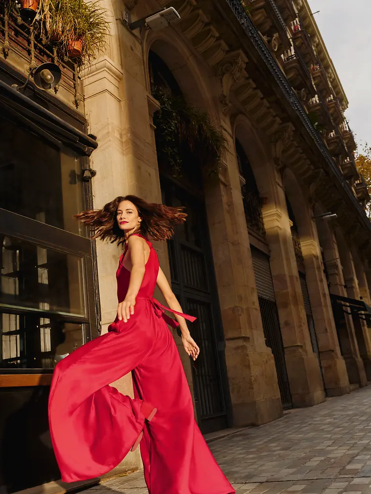 A woman wearing a red flowy jumpsuit is dynamically taking stairs while looking over her shoulder.