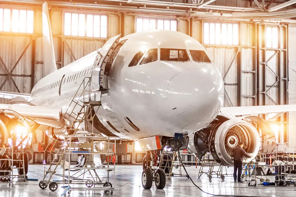 A large commercial airplane undergoing maintenance in a bright, spacious hangar.