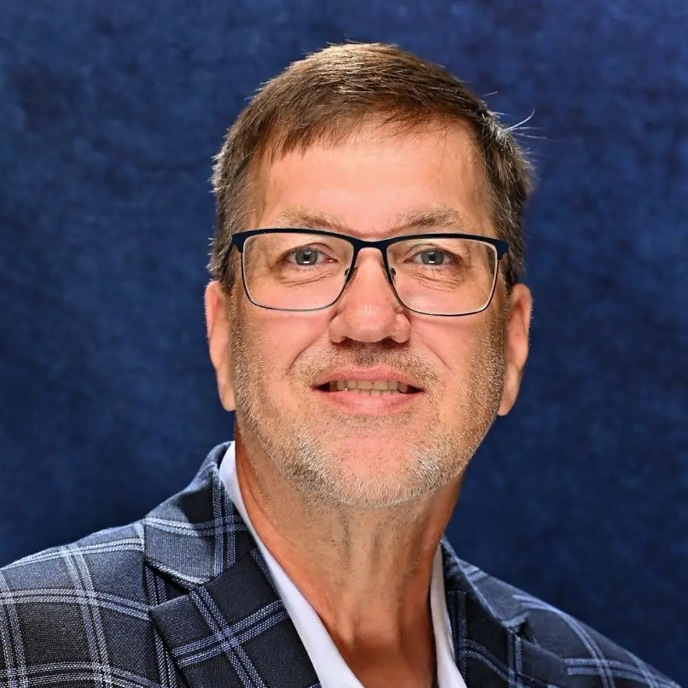 Bill smiling and wearing blue suit against blue background.
