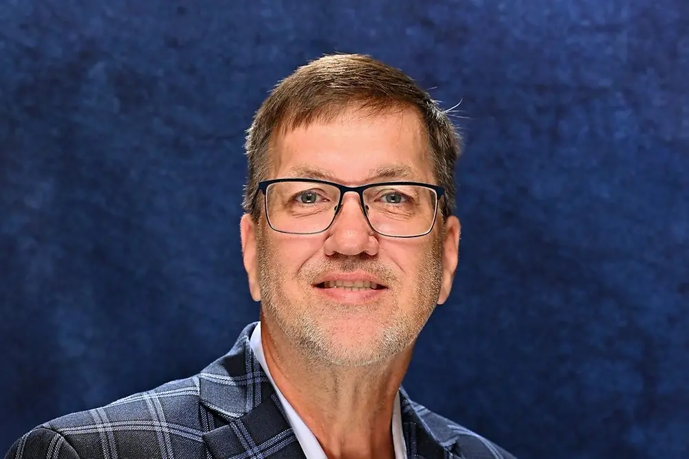 Bill smiling and wearing blue suit against blue background.