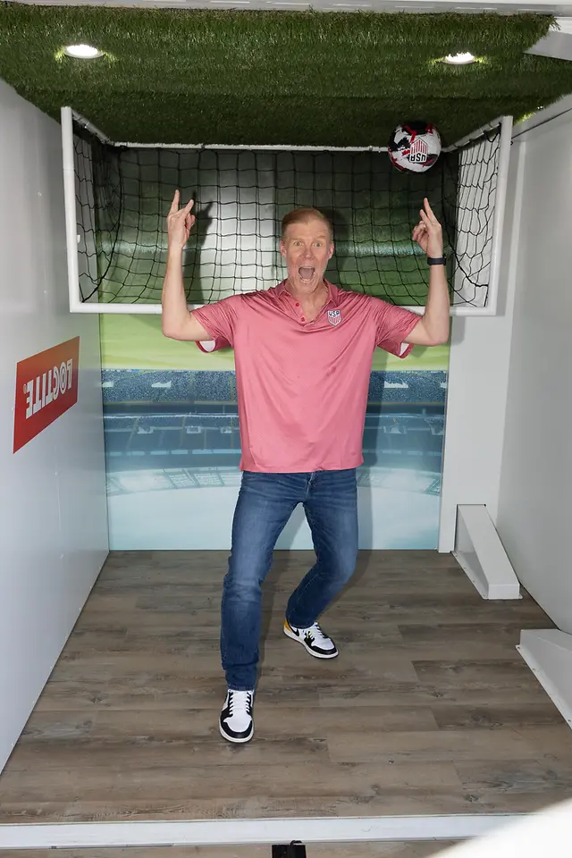 Alexi Lalas points to an upside down soccer pitch in the Loctite room in the Henkel House
