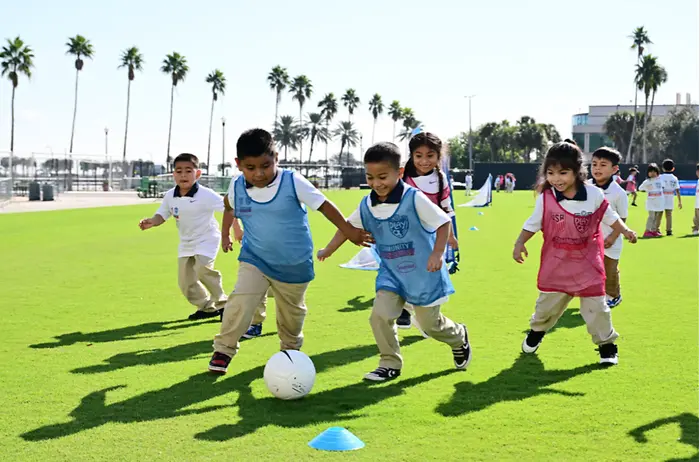 Children with blue and red vests playing with soccer ball on the field.