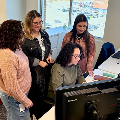 Group of women collaborating around a computer in the office.