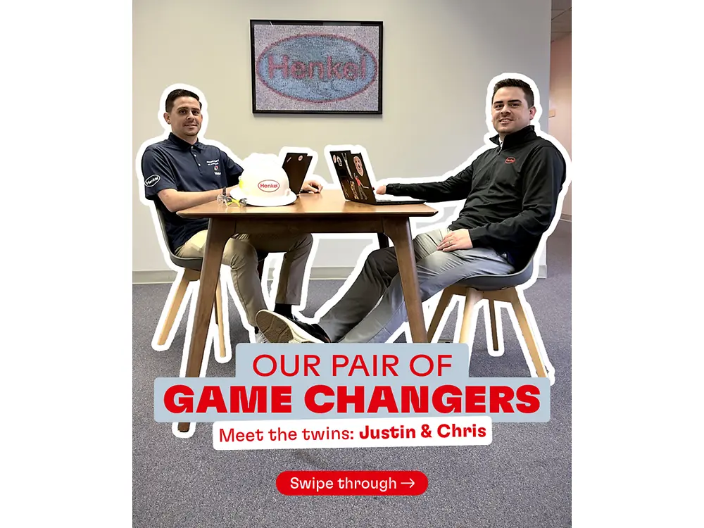 Two coworkers (who are also twin brothers) sit at a small table with laptops in an office. A Henkel logo is on the wall, with overlay text: ‘Our Pair of Game Changers – Meet the twins: Justin & Chris.