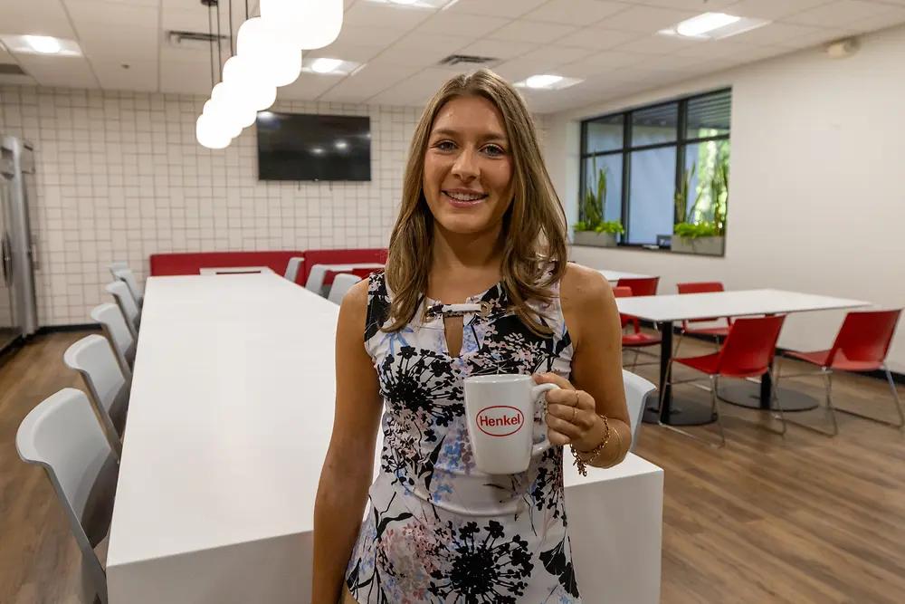 A photo of a female ACA employee holding a Henkel-branded mug.