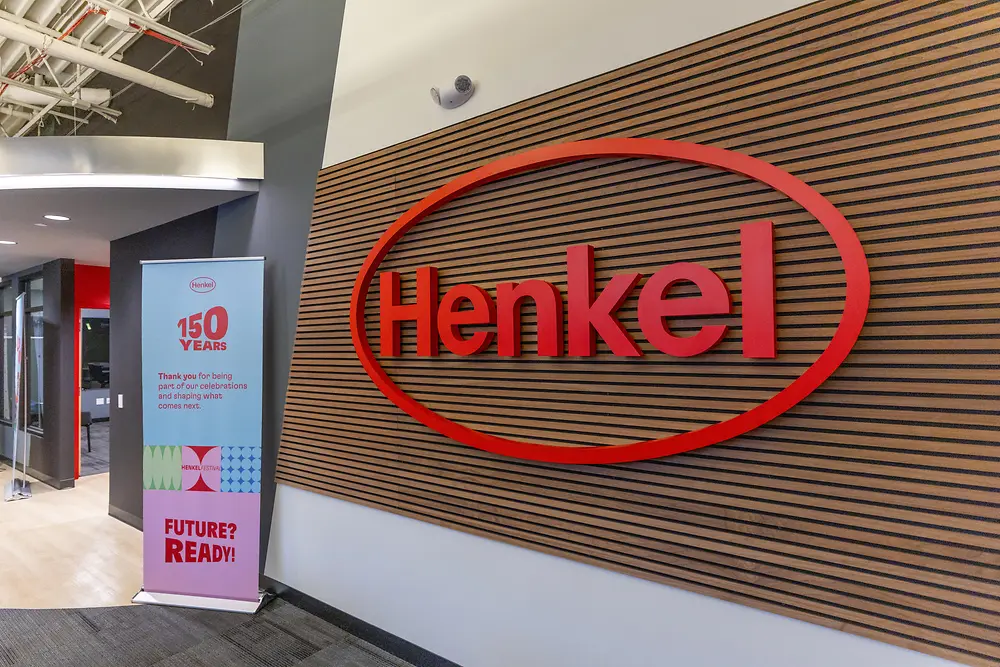 A photo of a Henkel building with a Henkel sign on the wall and a celebratory poster of the 150 years Henkel anniversary.