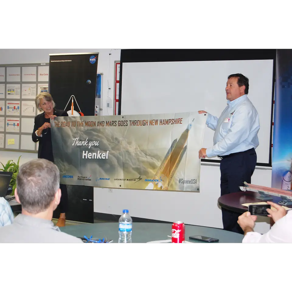 Marcia Lindstrom of NASA and Mark Olsen of OrbitalATK present Henkel with a commemorative banner for their partnership in creating materials used in NASA’s Space Launch System (SLS) project.