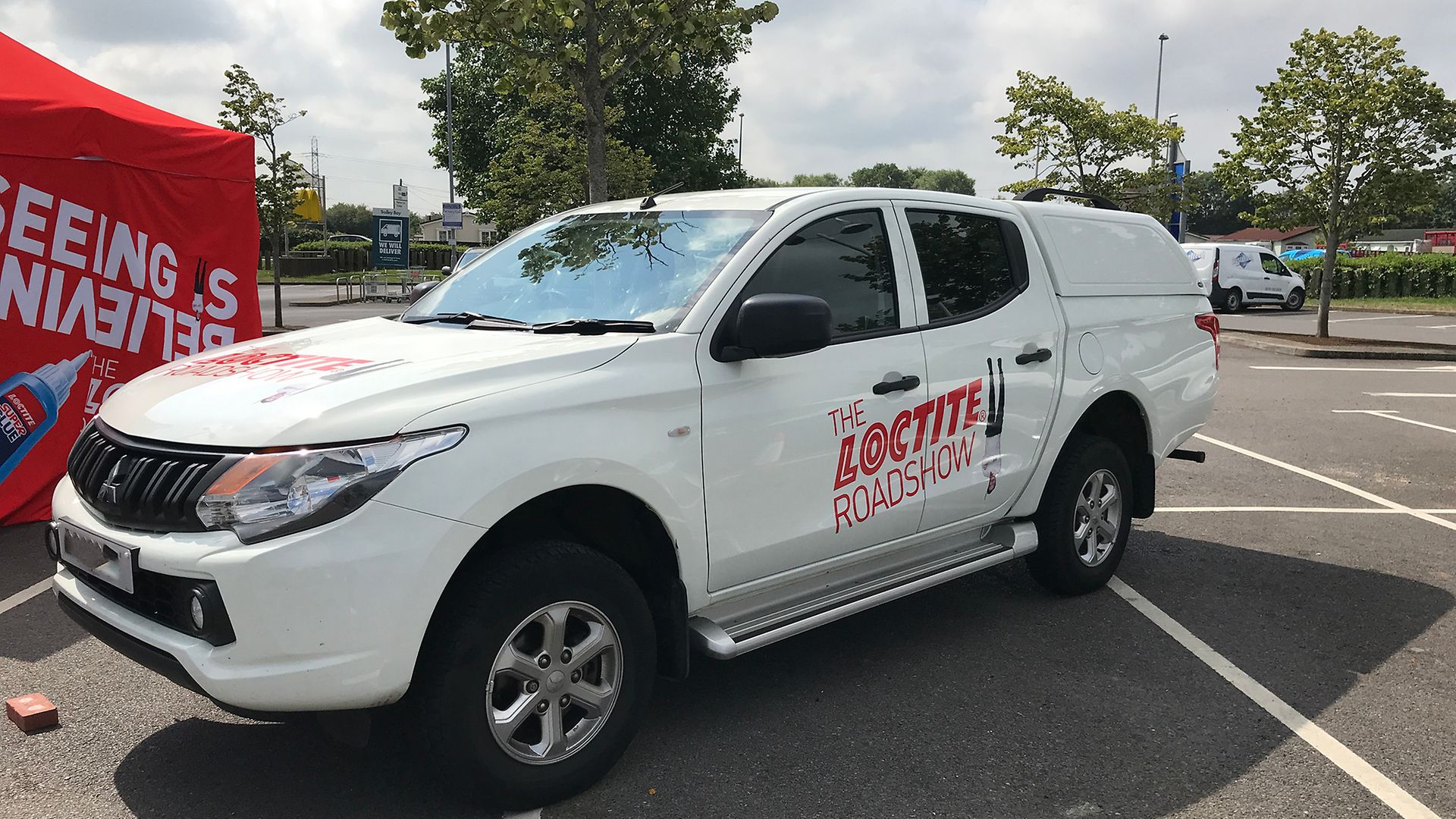 A white Mitsubishi SUV branded with 'The Loctite Roadshow' logo standing on a parking lot